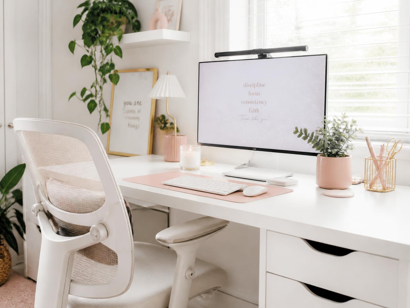 Bright feminine home office with an ergonomic chair, monitor, plants, and pastel desk accessories